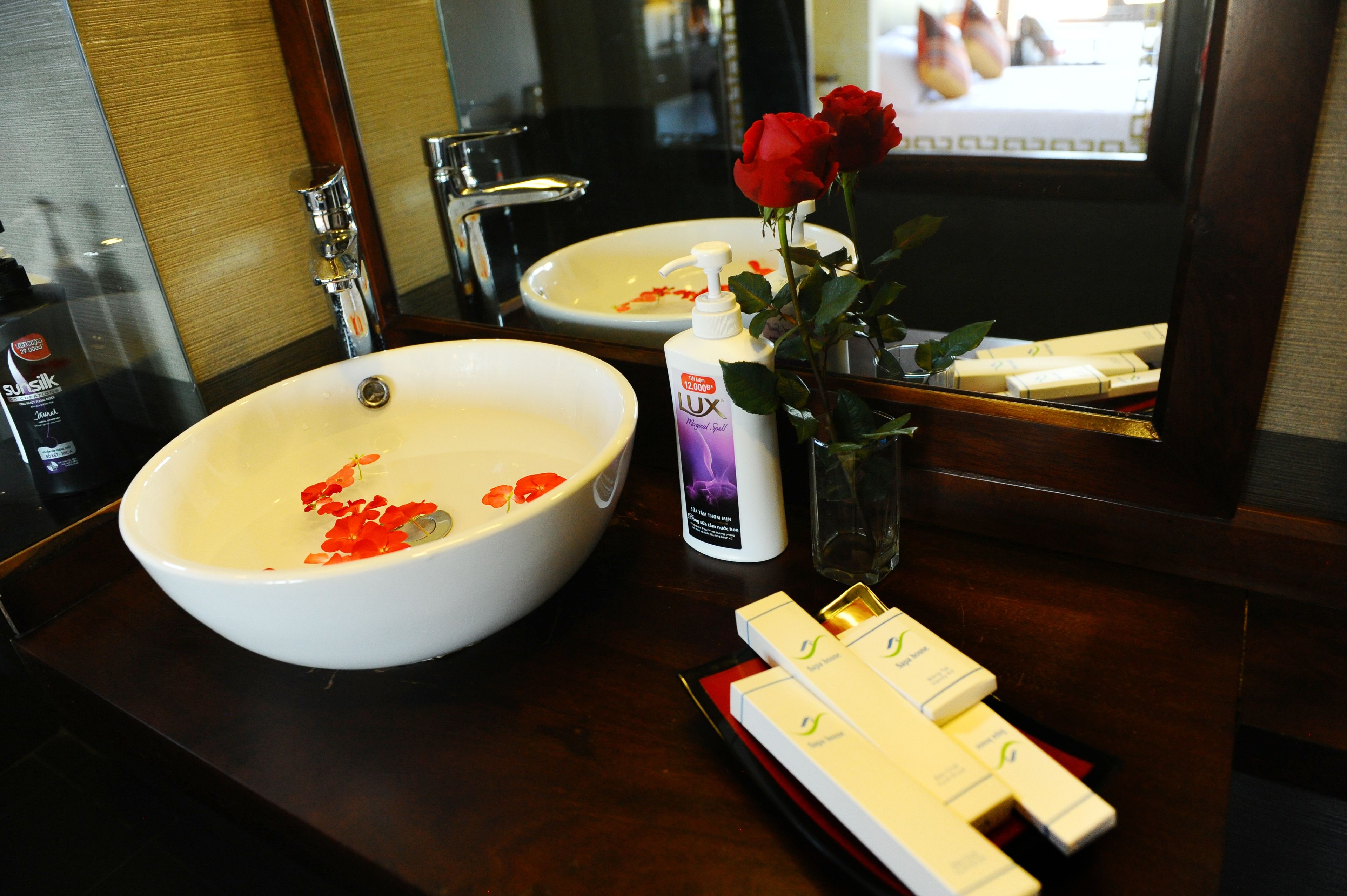 A bathroom with a large white sink, a mirror, and a bottle of Lux soap.