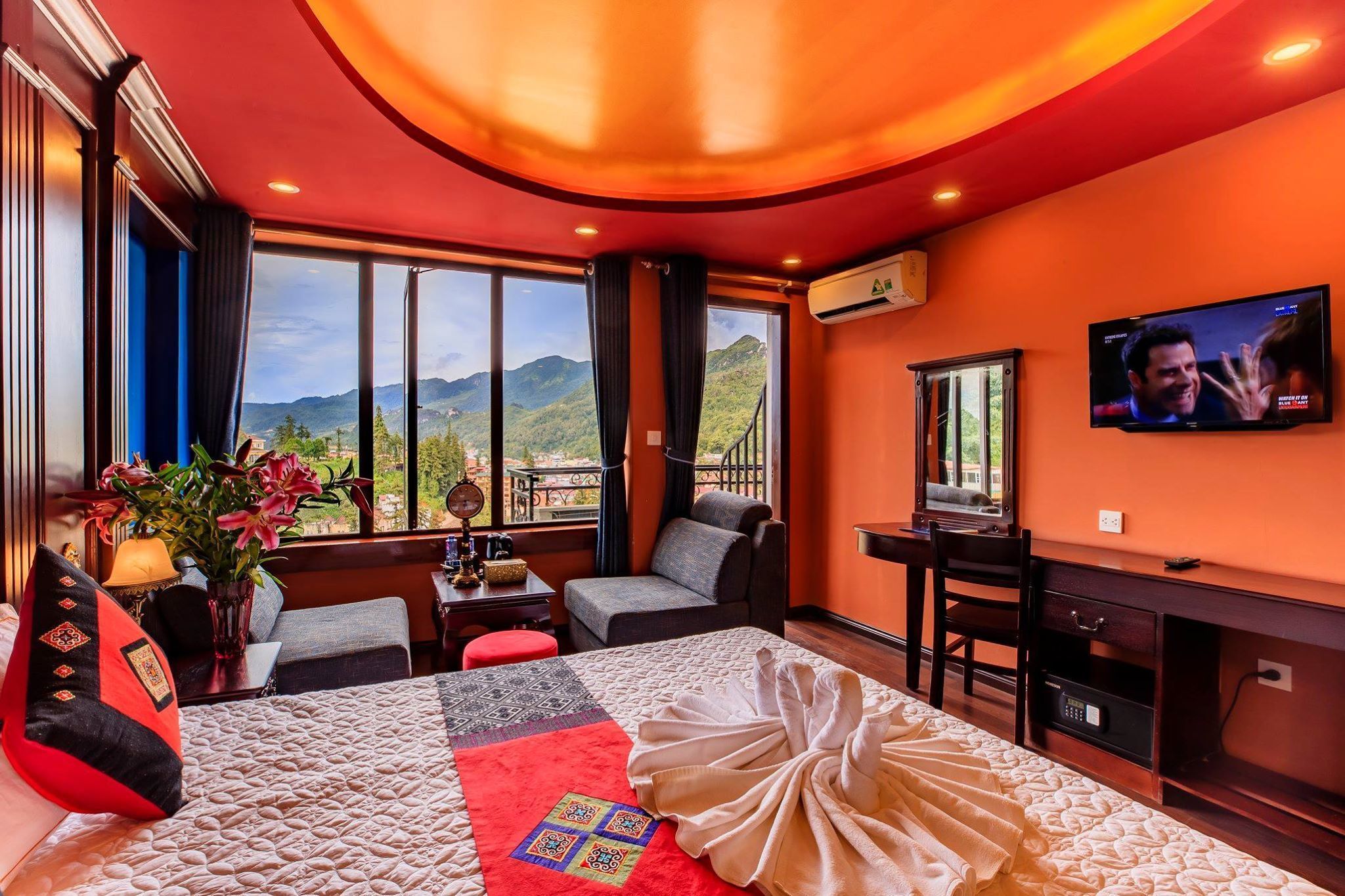 A hotel room with a large bed, a desk, a chair, a TV, and a view of mountains.