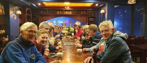 Um grupo de pessoas sentado em volta de uma mesa de madeira numa sala com parede azul e um candelabro.