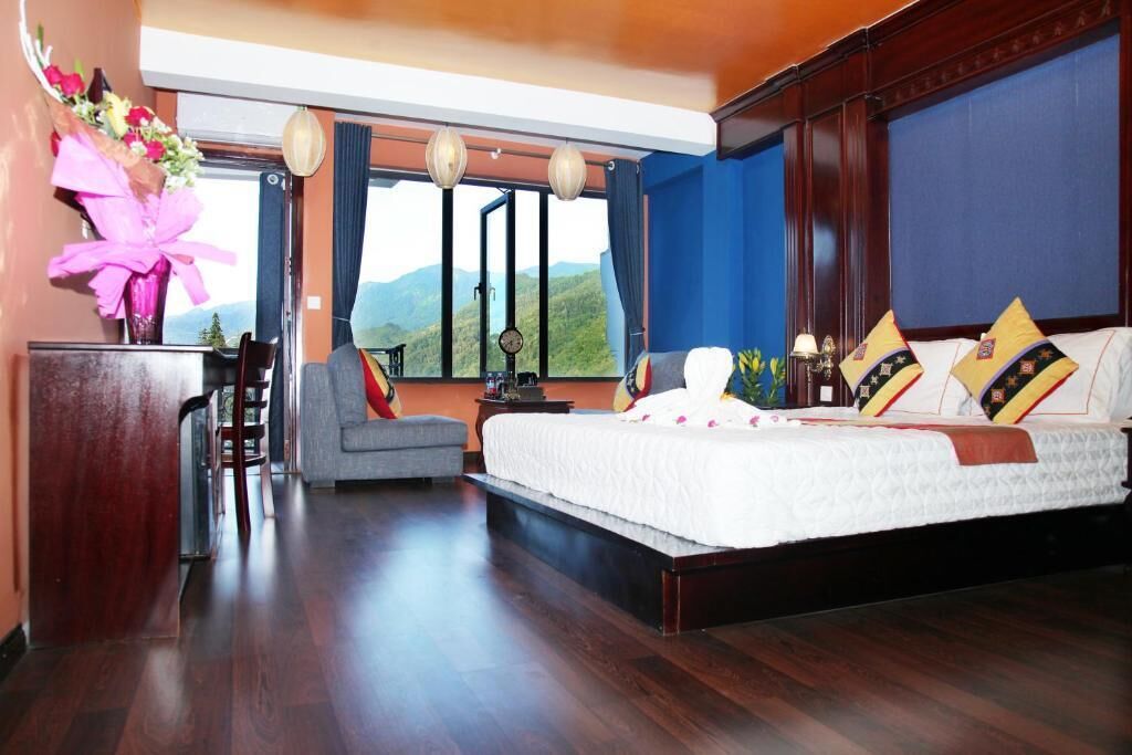 Une chambre avec un grand lit, un bureau et une chaise. Il y a une fenêtre d’où l’on peut admirer la vue sur les montagnes.