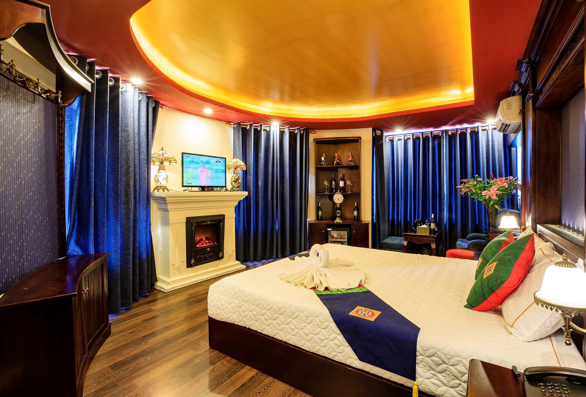 A hotel room with a large bed, a fireplace, a television, and a desk with a lamp.