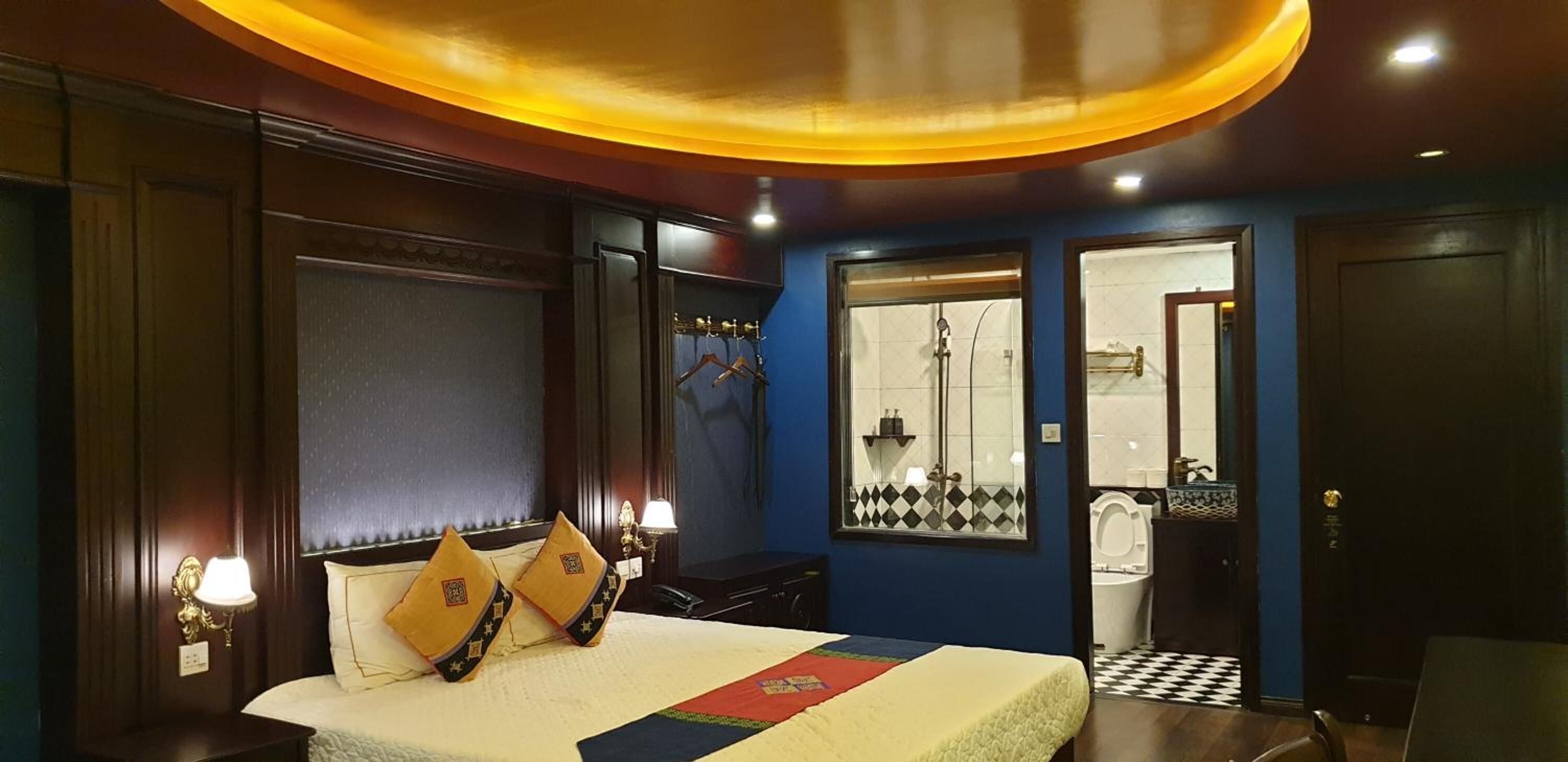 Habitación de hotel con cama, lámparas de noche, ventana con vistas, baño con inodoro y lavamanos, y una puerta.