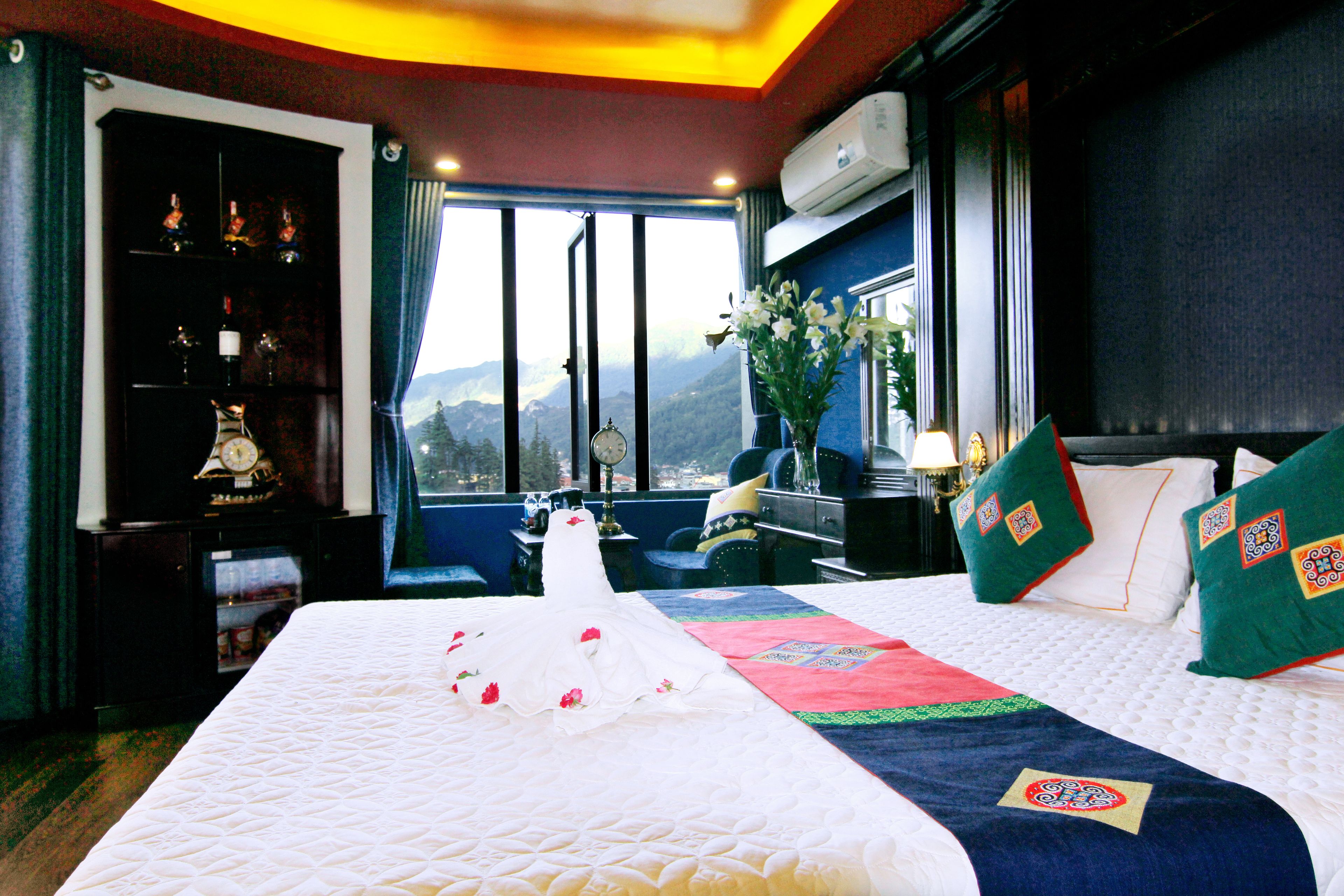 A hotel room with a large bed, a nightstand, a bookshelf, and a window with a mountain view.
