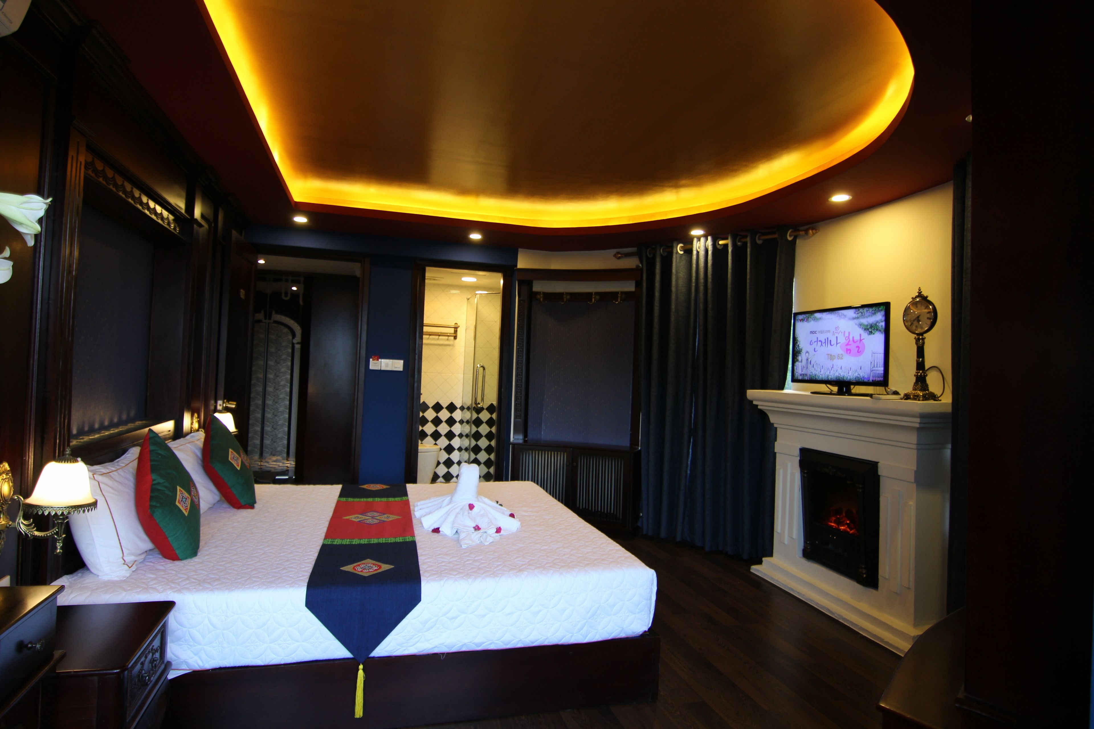 A hotel room with a large bed, a television, a fireplace, and a clock on the mantel.