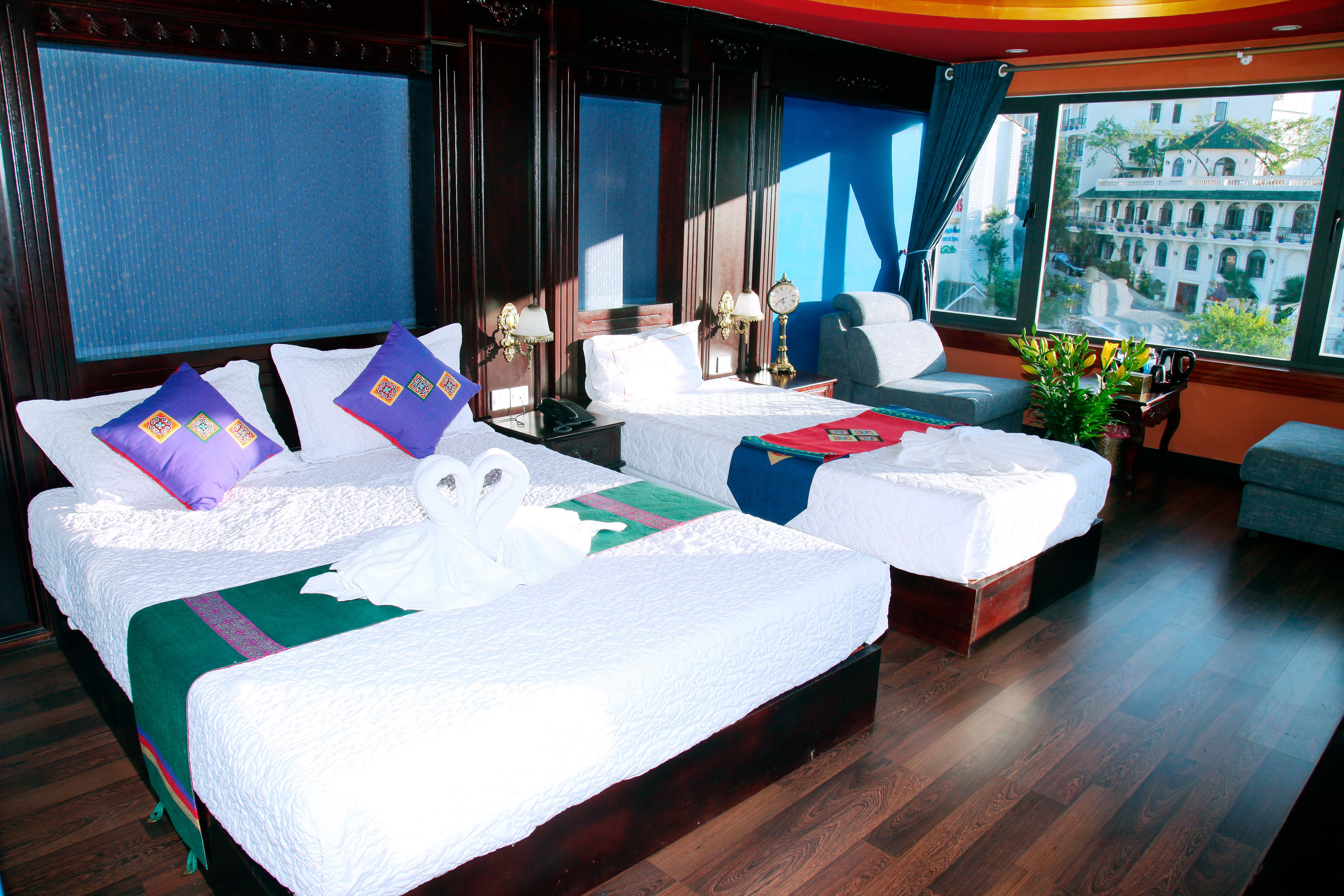 Habitación de hotel con dos camas, un sofá, vistas a un edificio y una ventana con cortinas.