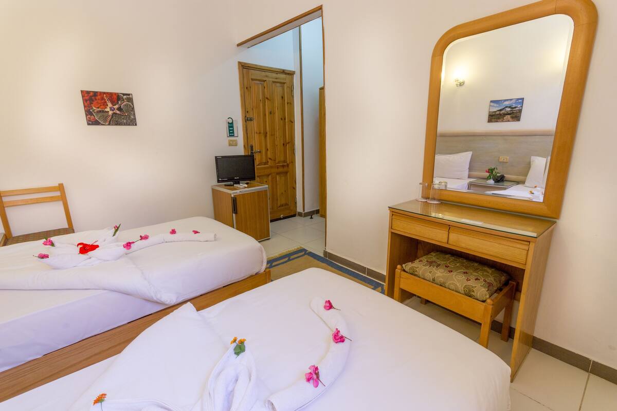 A hotel room with two beds, a wooden desk, a mirror, and a television.