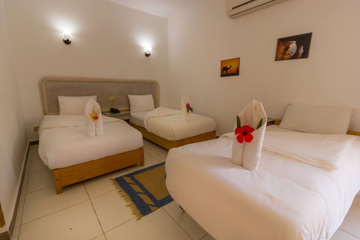 A hotel room with two beds, a nightstand, a wall-mounted lamp, and a small painting.