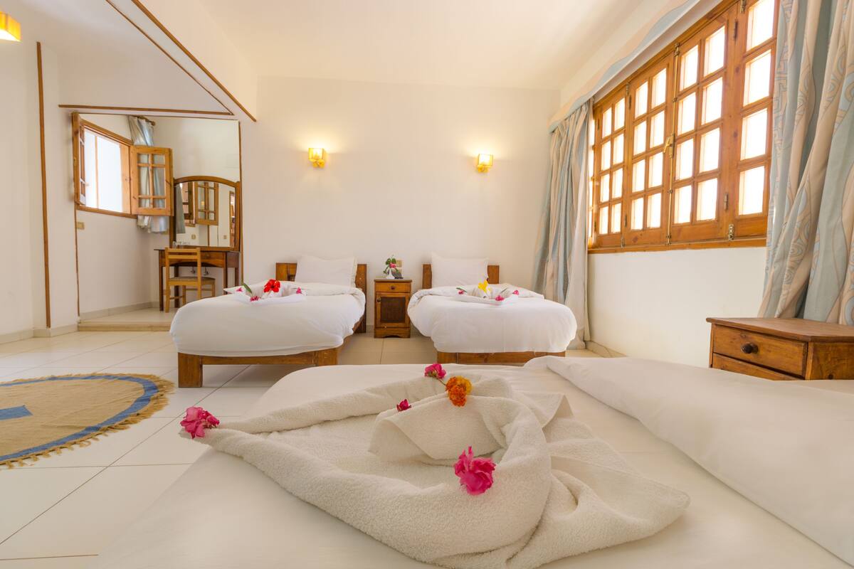 A hotel room with two beds, a sitting area, and a large window with curtains.