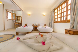 Habitación de hotel con dos camas, una zona de estar y un ventanal con cortinas.