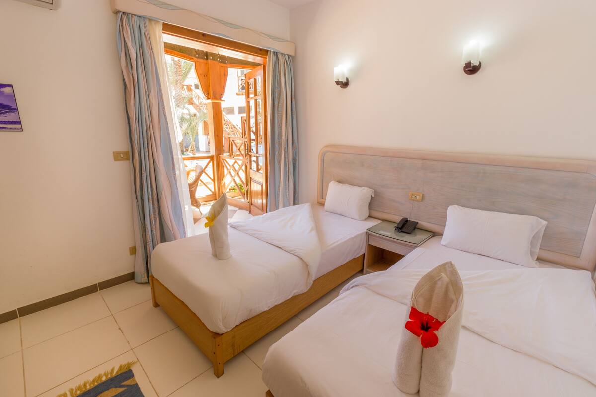 A hotel room with two beds, a wooden headboard, a nightstand, and a view of the outdoor area.