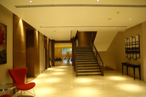A modern hotel lobby with a staircase, a red chair, and a wooden bench.