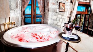 Ein Zimmer mit einer großen Badewanne, gefüllt mit Wasser und roten Rosenblüten, einer Weinflasche und zwei Weingläsern auf einem Tisch.