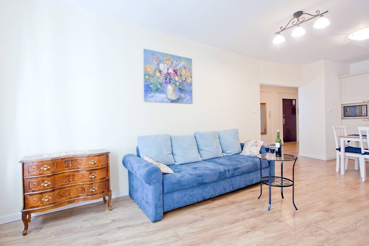 Een woonkamer met een blauwe bank, een houten dressoir en een schilderij aan de muur.
