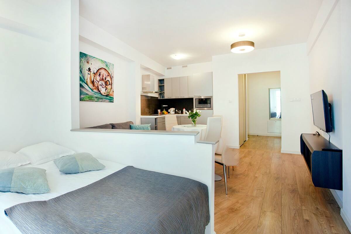 Een moderne hotelkamer met een bed, nachtkastje, lamp en een schilderij aan de muur.
