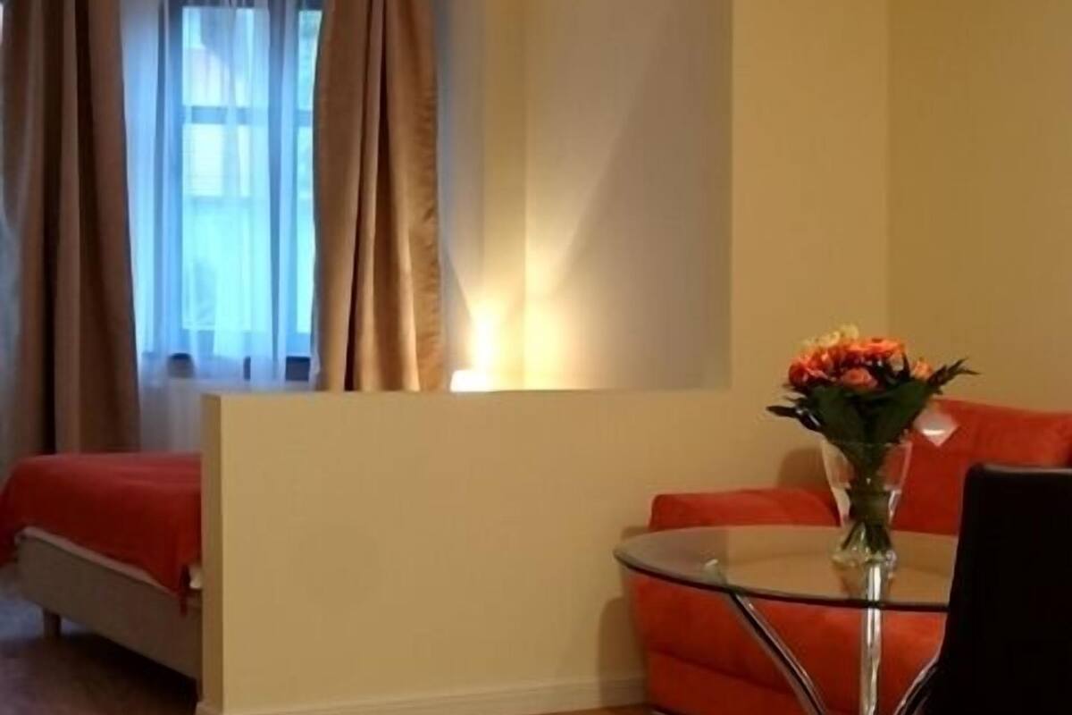Een moderne kamer met een bed, een glazen tafel met een bloemetjesvaas, een rode bank en een zwarte stoel.