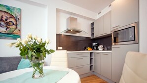 A modern kitchen with grey cabinets, a built-in microwave, and a vase of white flowers on the dining table. - Apartamenty Centrum Villa Perla (Jelenia Gora)