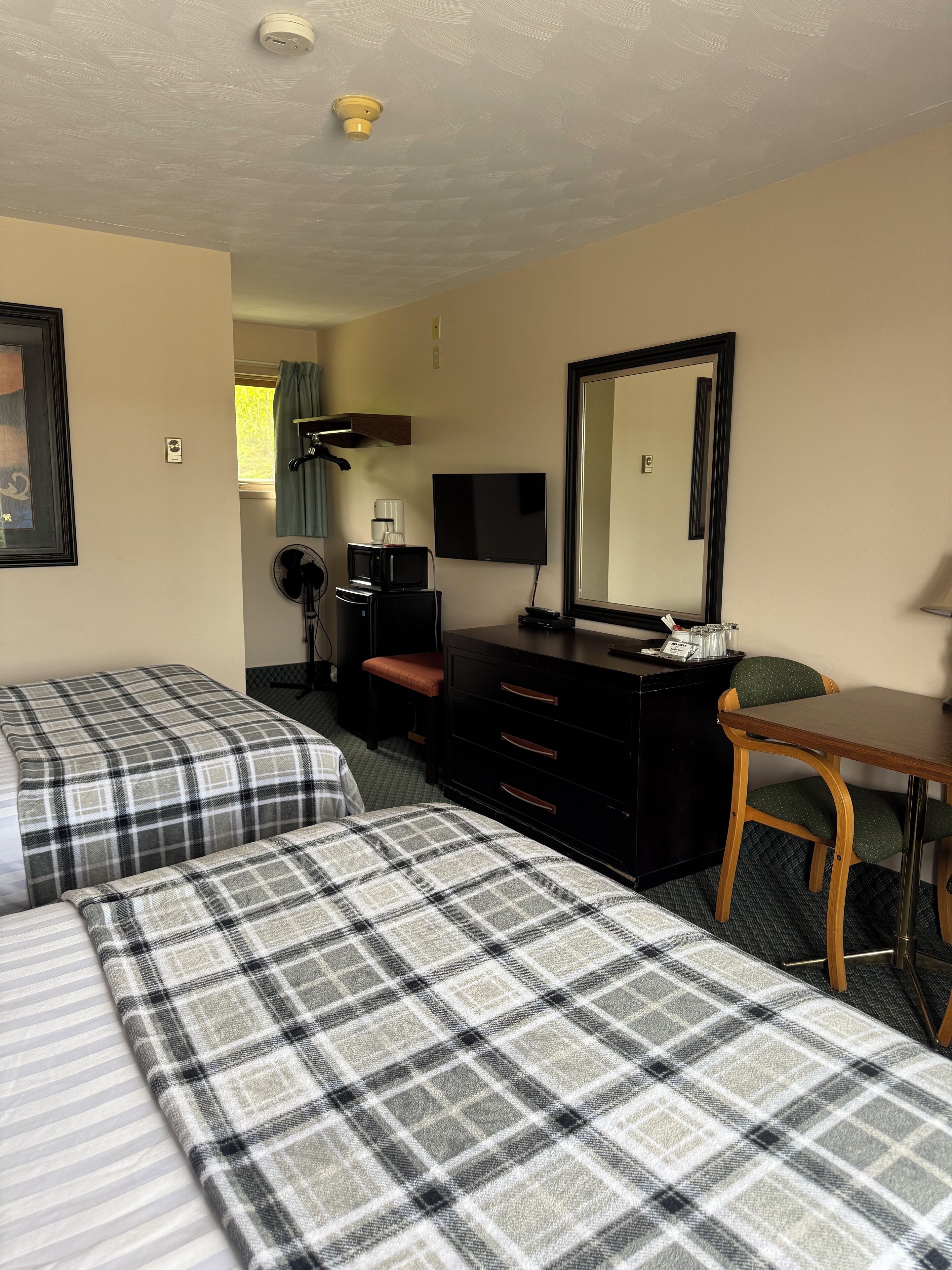 A hotel room with two beds, a dresser, a mirror, a TV, and a desk.