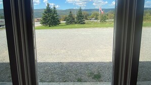 Une vue à travers une fenêtre dont le cadre est en métal, donnant sur un espace recouvert de gravier, avec des arbres et un drapeau.