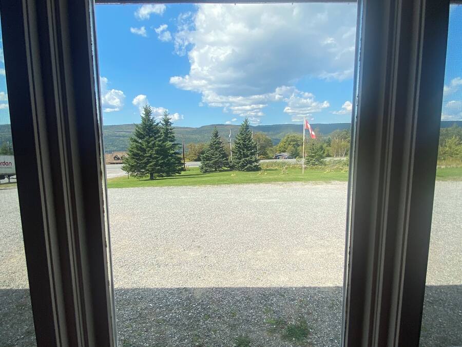 A view through a window with a metal frame, looking out to a gravel area with trees and a flag.