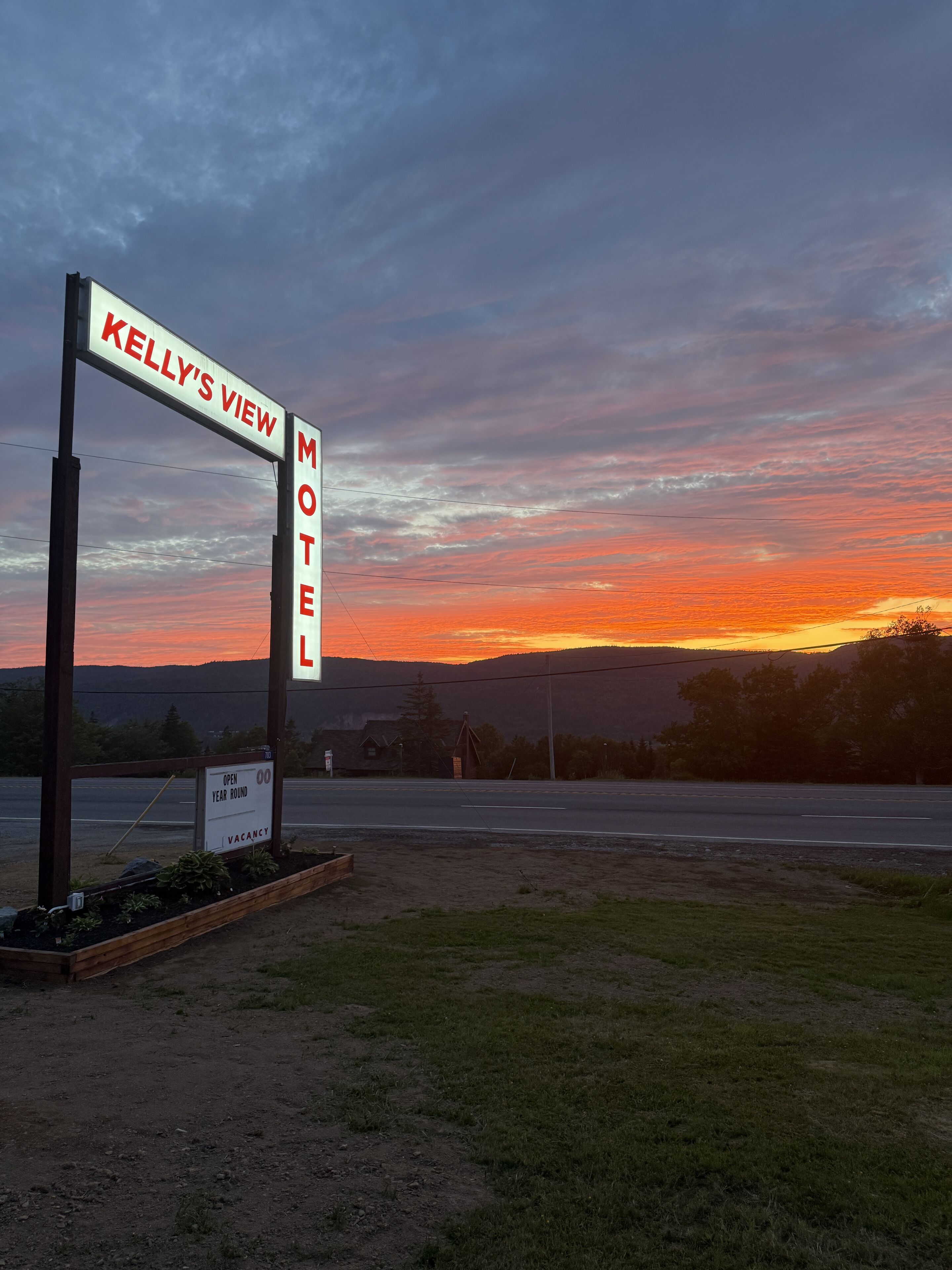 Een motelbord met daarop 'Kelly's View' en 'Motel' vermeld, een bord met 'Geopend het hele jaar door' en 'Kamers beschikbaar', en een weg op de voorgrond.
