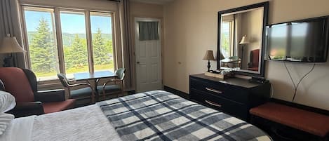 Habitación de hotel con una cama grande, un escritorio, una silla, un televisor y una ventana con vistas a árboles y una carretera.