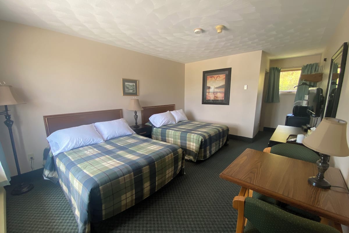 Habitación de hotel con dos camas, un escritorio, una silla, una lámpara, un cuadro y una ventana con cortinas.