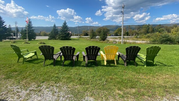 Un espace extérieur verdoyant, avec plusieurs fauteuils Adirondack disposés en rangée, face à un paysage pittoresque de montagnes et d’une route.