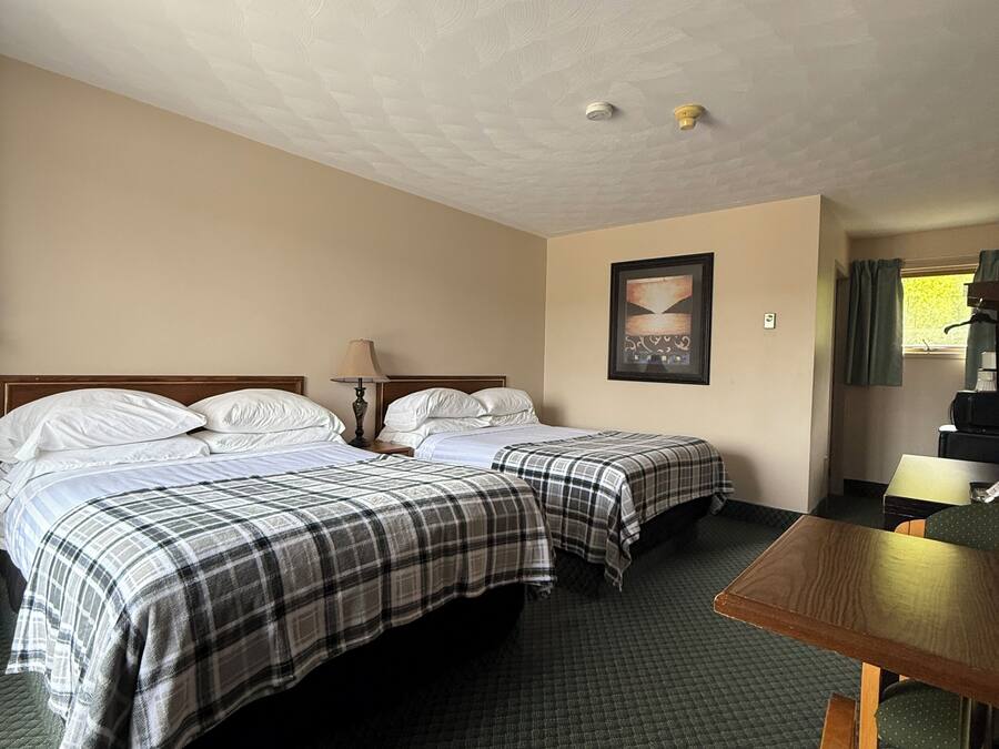 Een hotelkamer met twee bedden, een tafeltje, een stoel, een schilderij aan de muur en een raam met gordijnen.