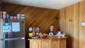 Un comptoir d’accueil avec un réfrigérateur rempli de boissons, un panier de collations et un menu.