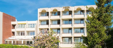 A multi-story hotel with a flat facade, balconies, and a well-maintained garden.