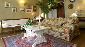 Een woonkamer met een bloemenbank, een witte tafel met een bloevas, een houten bankje en een kamerbreed tapijt.