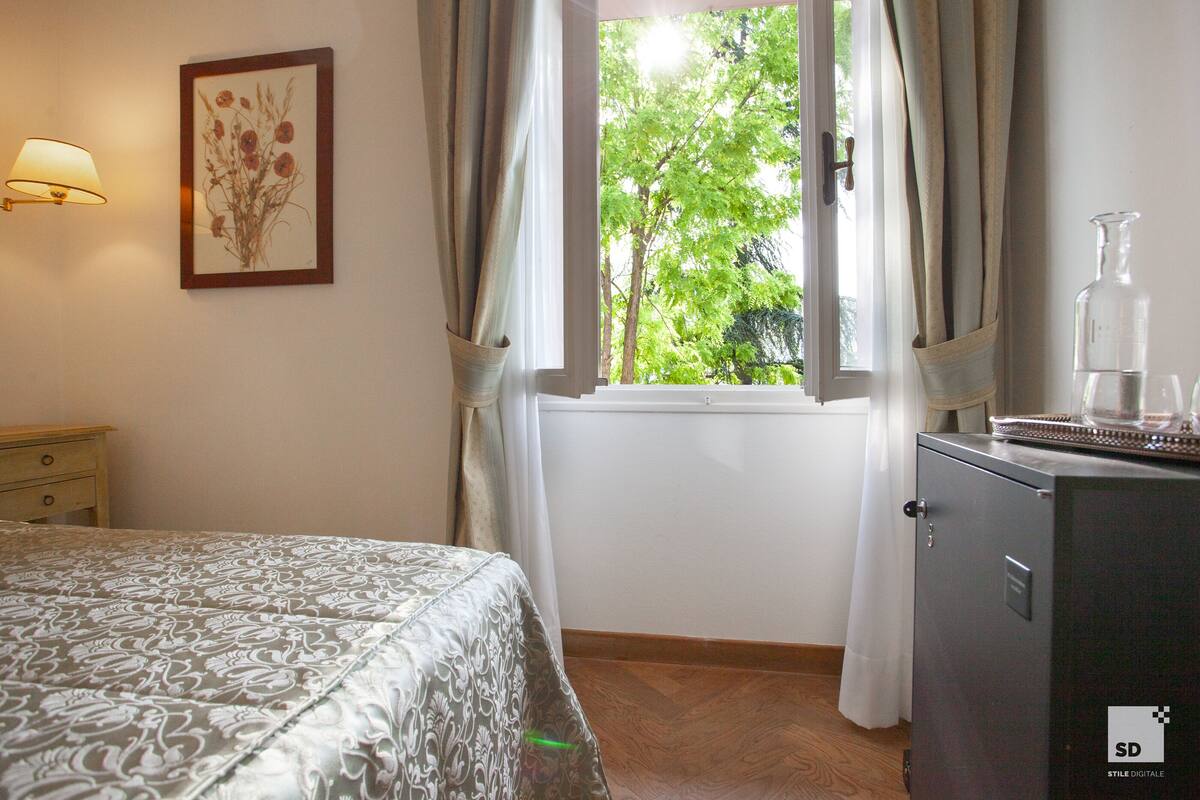 Een slaapkamer met een bed, nachtkastje, lamp, raam met gordijnen en een kast.