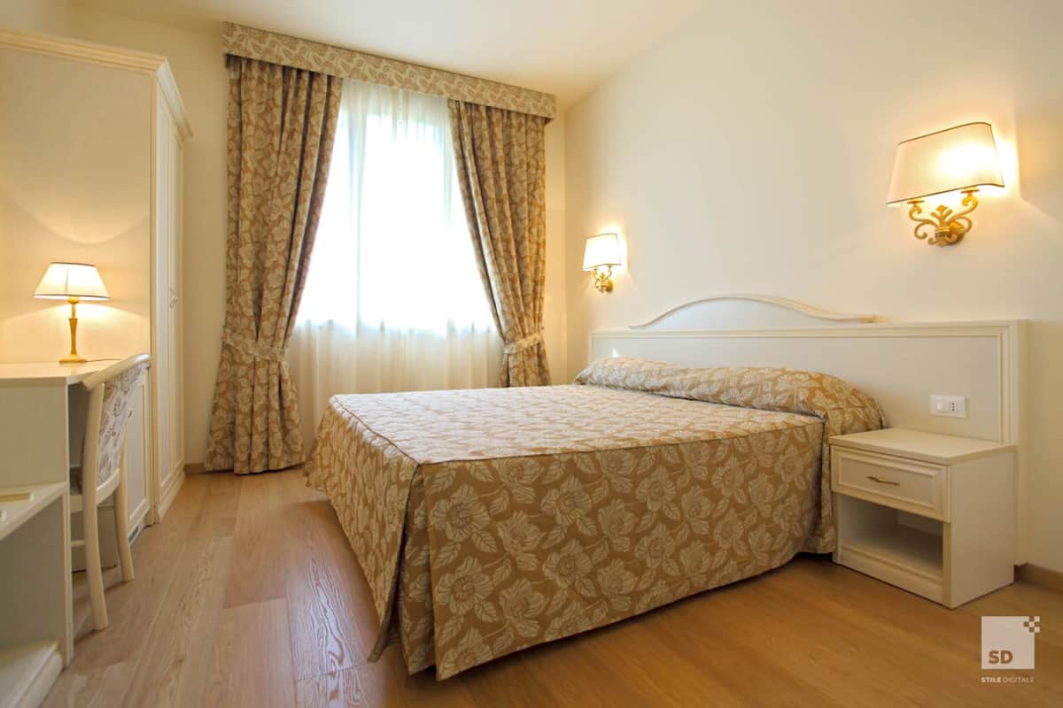 Een hotelkamer met een bed, nachtkastjes, een bureau en een raam met gordijnen.