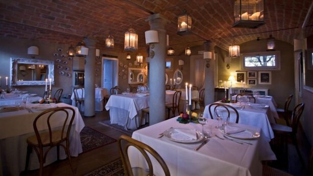 Een restaurant met bakstenen muren, witte tafellakens en kaarslicht op de tafels.