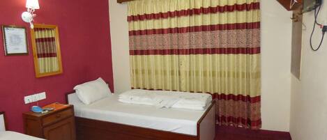 A hotel room with a bed, a nightstand, a lamp, a television, and a window with curtains.