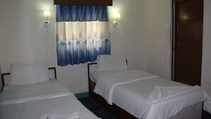 A room with two single beds, a window with a blue curtain, and two wall-mounted lamps.
