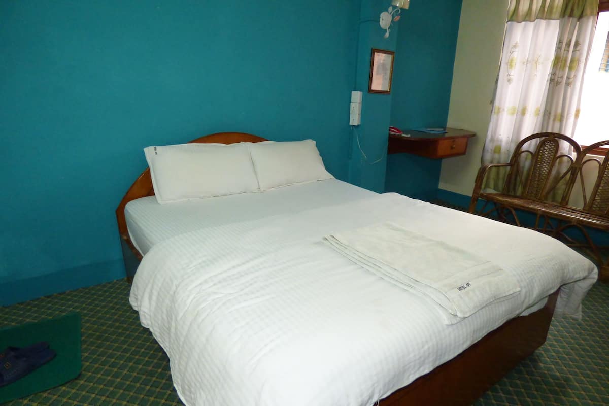 A neatly made bed with white linens in a room with teal walls and a checkered floor.