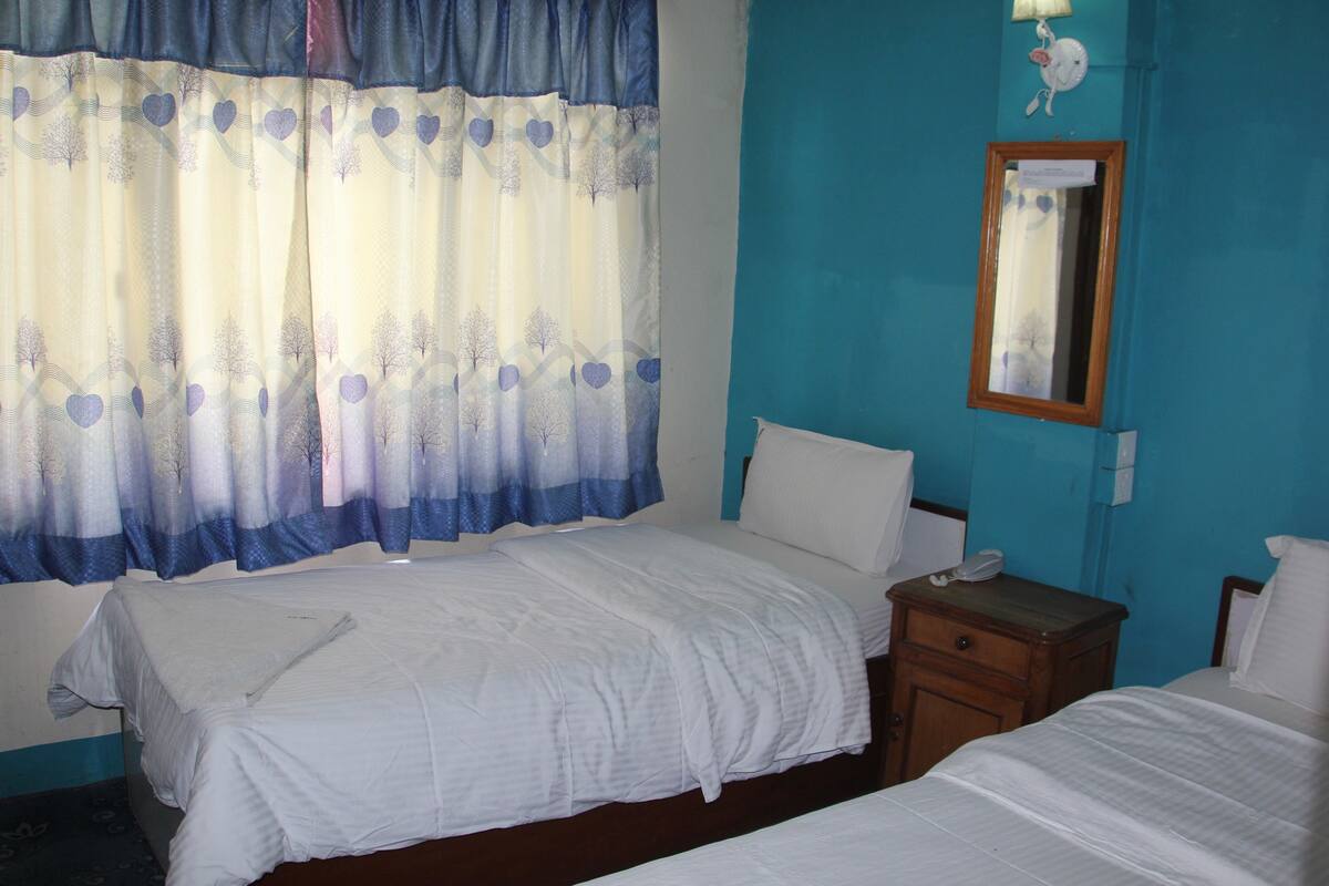 A hotel room with two beds, a nightstand, a mirror, and a wall-mounted lamp.