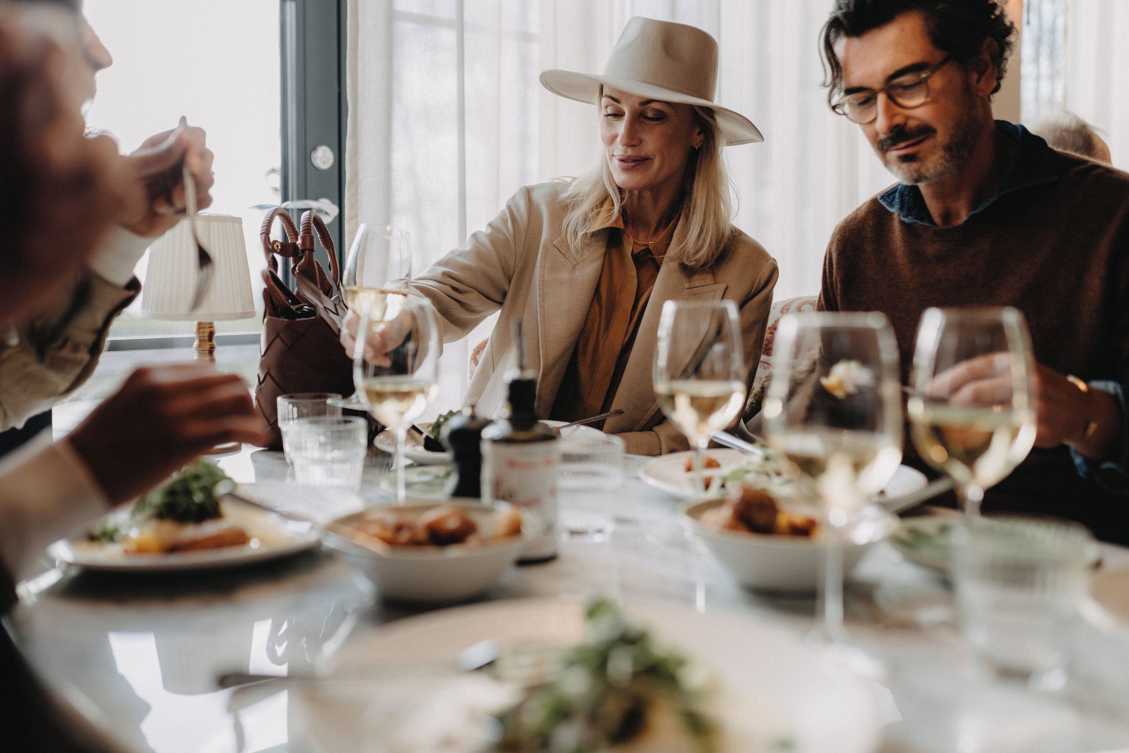 Un grupo de personas cenando en una mesa con diferentes platos y copas de vino.