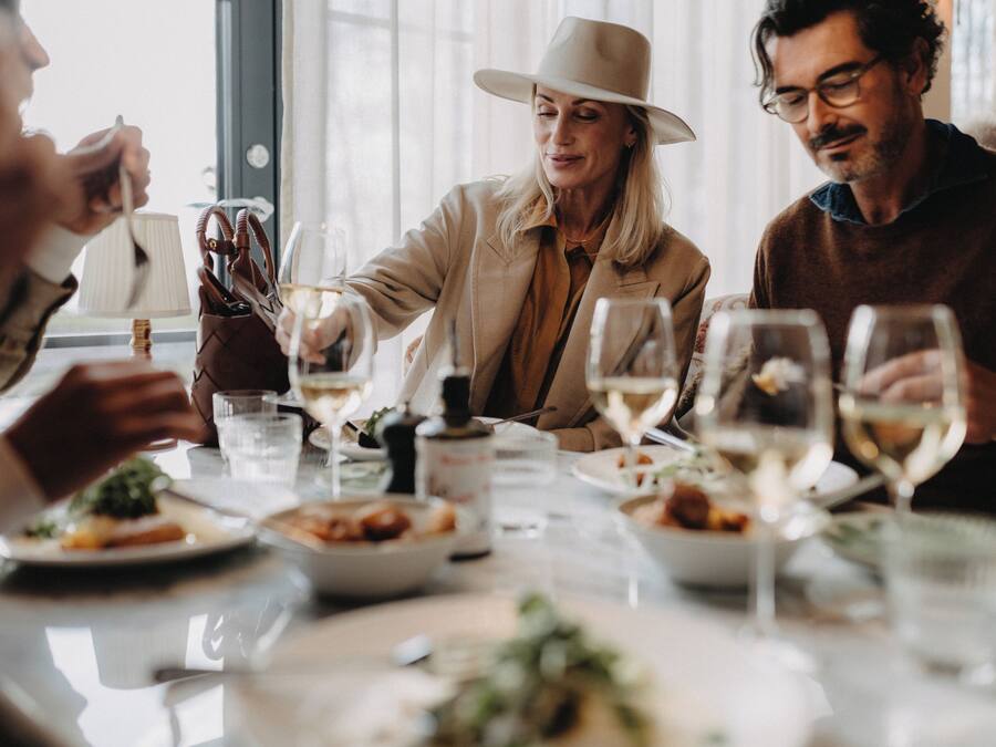 A group of people dining at a table with various dishes and glasses of wine.