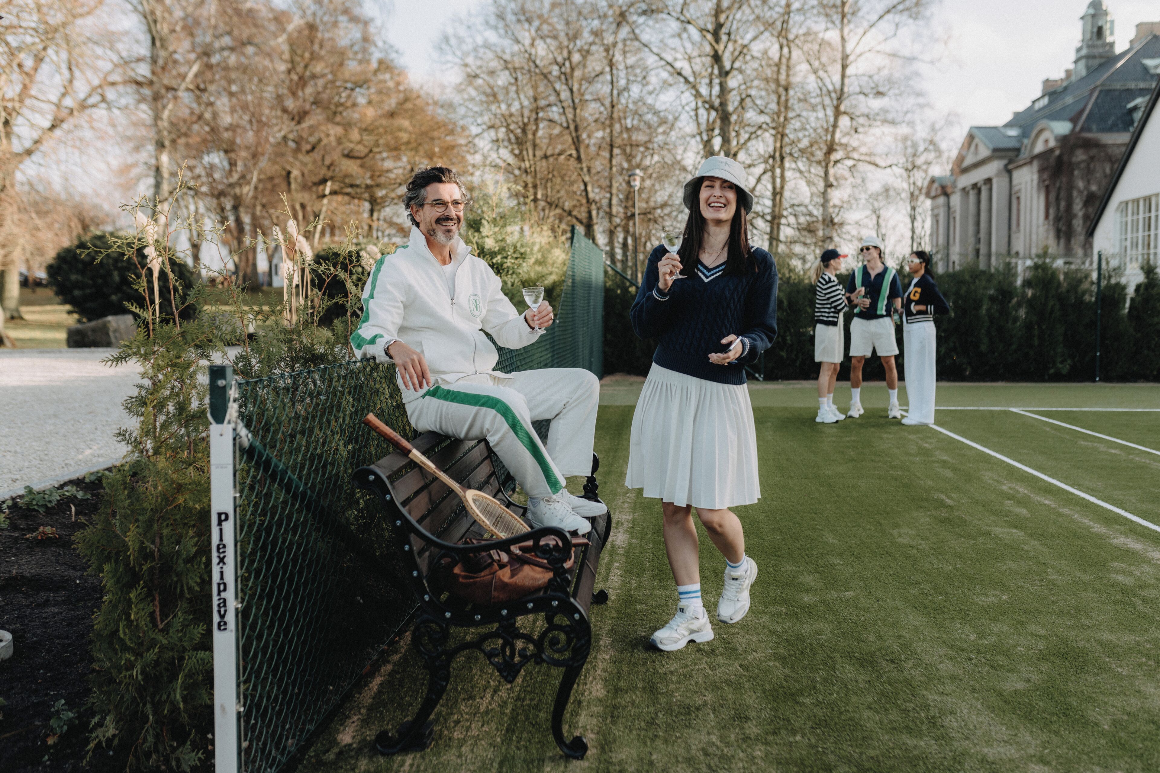 Een bank met een tennisracket en tas, een gazon en een gebouw op de achtergrond.