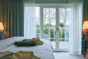 Habitación de hotel con cama, vista a través de un ventanal y lámpara en una mesita de noche.