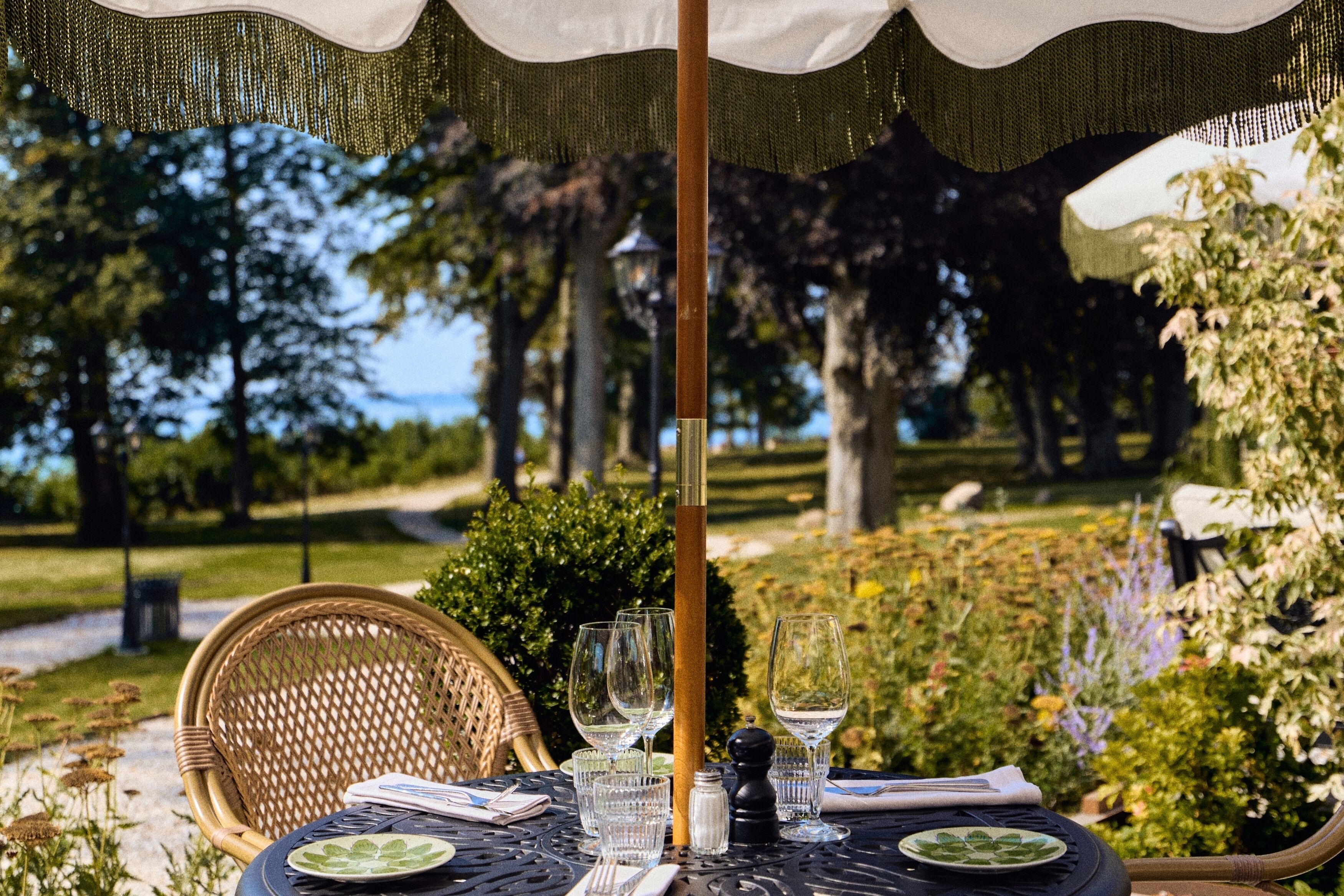 Une table à manger extérieure avec des chaises, un parasol et une vue sur un jardin et des arbres.