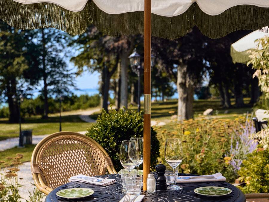 Une table à manger extérieure avec des chaises, un parasol et une vue sur un jardin et des arbres.