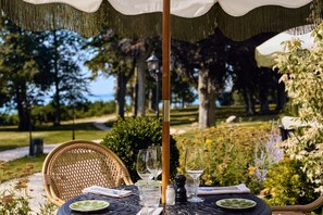 Mesa de comedor exterior con sillas, una sombrilla y vistas a un jardín y árboles.