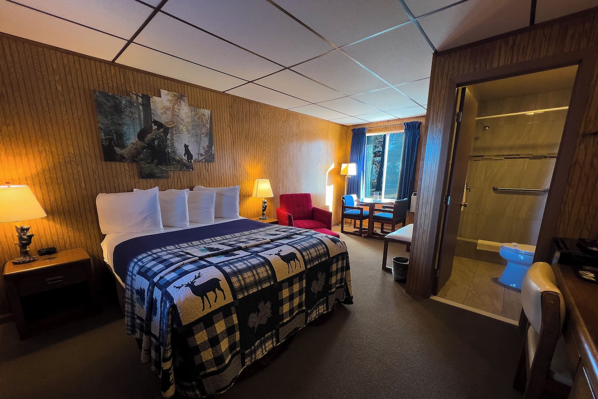 A hotel room with a large bed, a desk with two chairs, a shower area, and a painting on the wall.