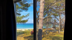A view through a window of a beach with trees and a clear sky. - Riviera Motel (Mackinaw City)