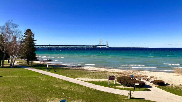 A coastal view with a bridge, grassy areas, and a pathway leading to the beach. - Riviera Motel (Mackinaw City)