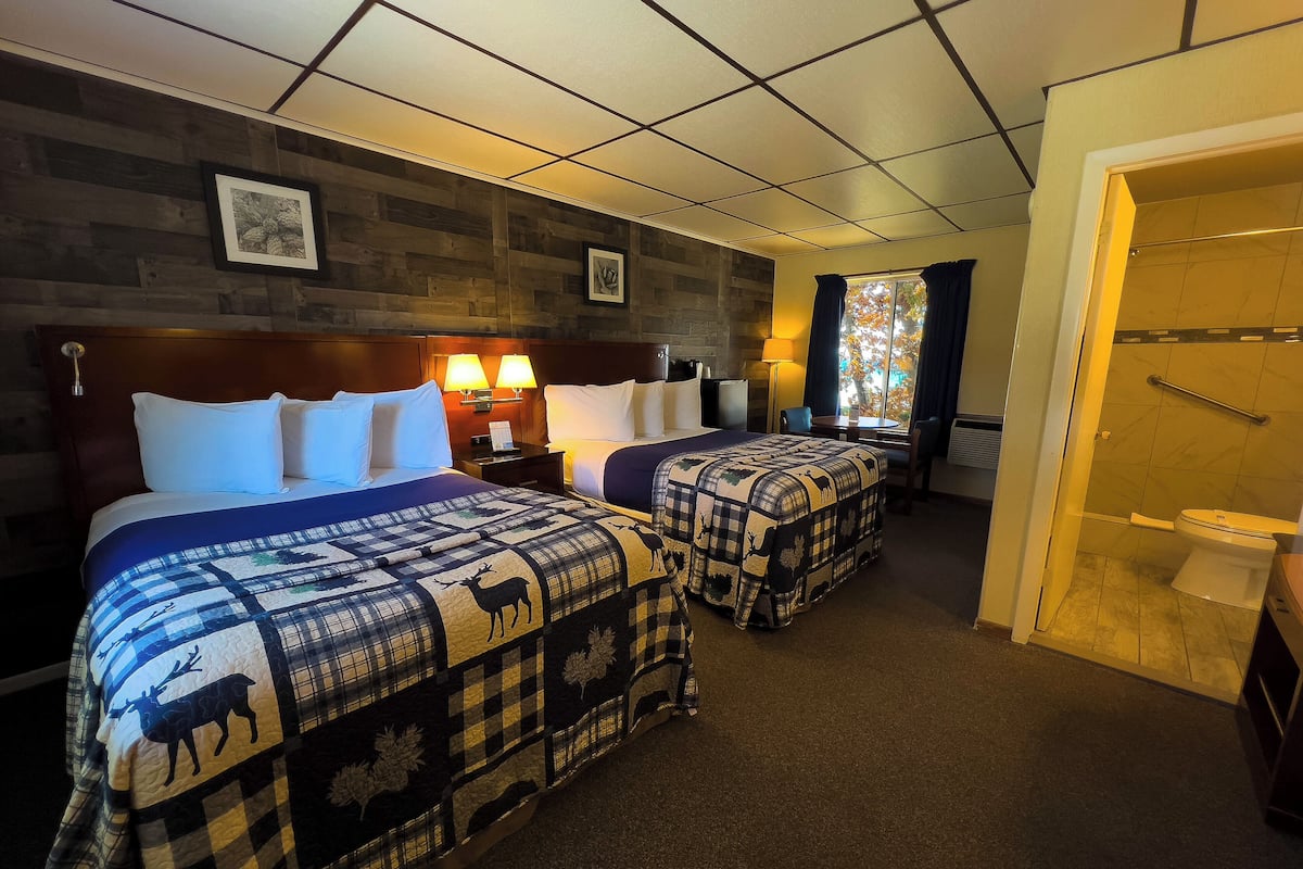 A hotel room with two beds, a desk, and a shower area.