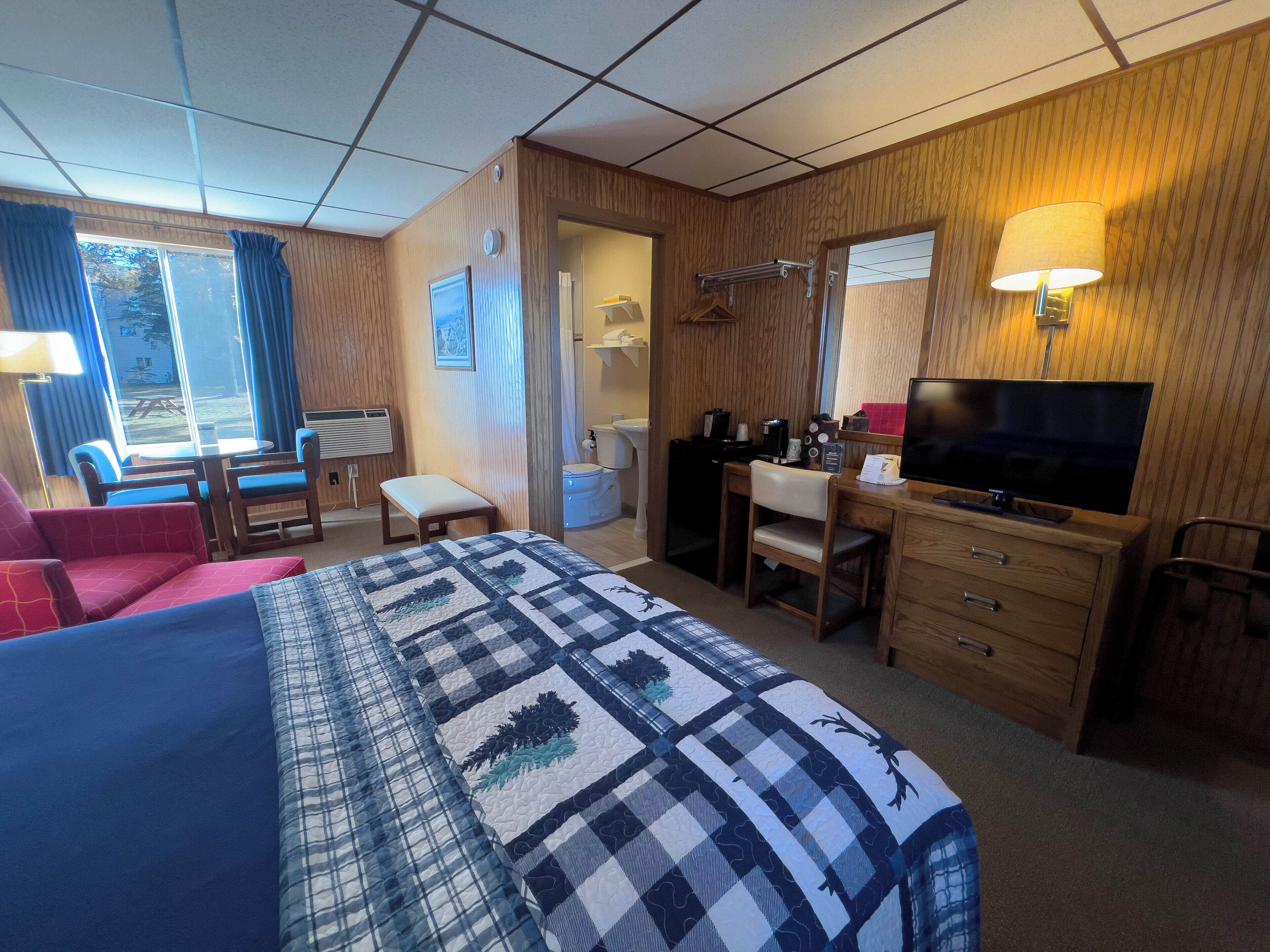 A hotel room with a bed, a desk, a chair, a TV, and a window with curtains.